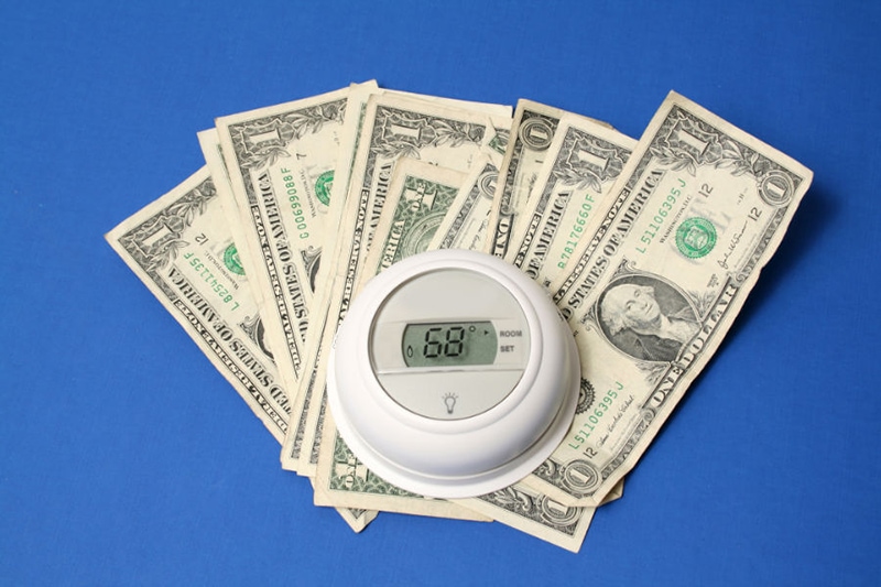 Spring Money-Saving Tips. Thermostat sitting on top of  bills.