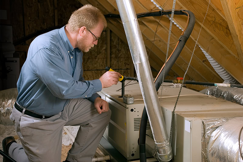 7 Furnace Maintenance Tips. Photo of a Technician in an attic attending to furnaces installed.