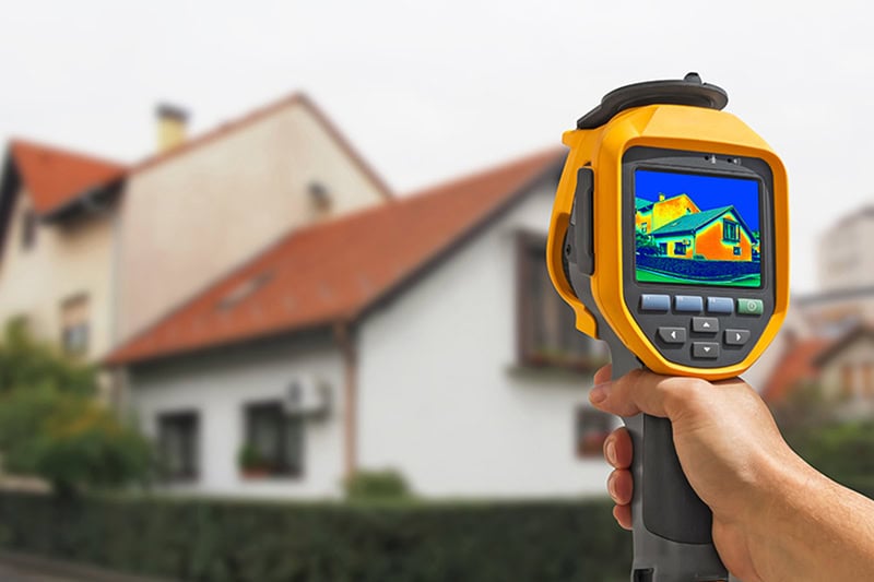 Hand holding a device to read energy output of a home in the background.